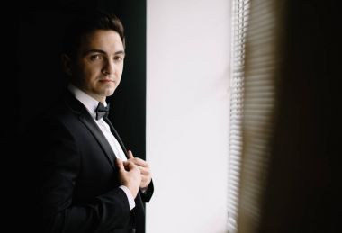 Gecenin düğün için hazırlanıyor süre pencerenin şık damat portre. lüks erkek takım papyon odada poz ile kendine güvenen bakışla. metin için yer.