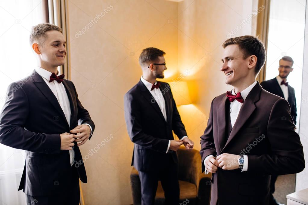 stylish groom laughing and having fun with groomsmen while getting ready in the morning for wedding ceremony. luxury man