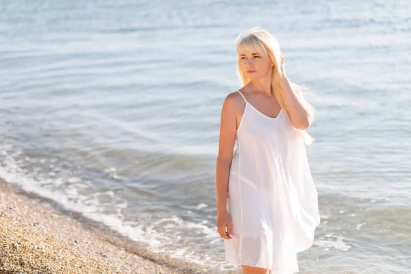 Belle femme blonde en robe blanche et chapeau de paille sur la plage — Photo