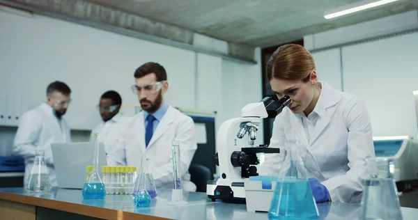 Eine Kaukasische Wissenschaftlerin Weißen Gewand Schaut Ins Mikroskop Während Sie — Stockfoto