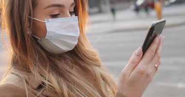 Tıbbi maske takan, mesaj atan ve caddede cep telefonunu dinleyen beyaz bir kadın. Boş bir şehirde akıllı telefondan yazı yazan ve kaydıran bir kız. Salgın konsepti.