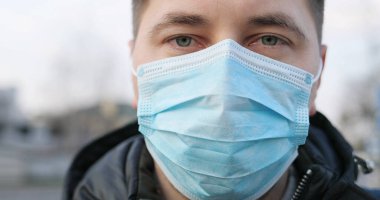 Sokakta dikilip kameraya bakan, tıbbi maskeli, üzgün, üzgün, beyaz bir adama yaklaş. Şehirde koronavirüsten korunan bir adamın portresi. Salgın hastalık konsepti. Temiz havada korunan kişi.