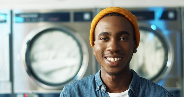 Primer plano de alegre joven afroamericano sonriendo a la cámara en la sala de servicio de lavandería . — Foto de Stock