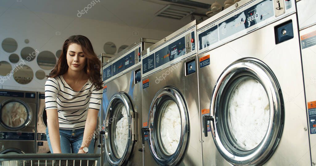 Cheerful Caucasian young beautiful woman having fun and laughing as throwing clothes from basket at laundry service.
