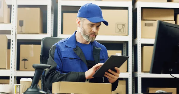 邮电局投递人员穿着制服 帽子在平板设备上工作的形象 男性信使填写发票并在电脑屏幕上输入数据 — 图库照片