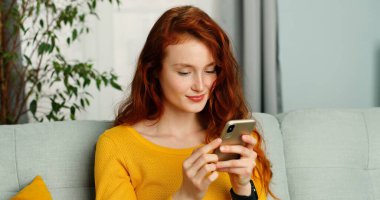 Güzel, kızıl saçlı, kıvırcık saçlı, akıllı telefonundan mesaj atan bir kadın..