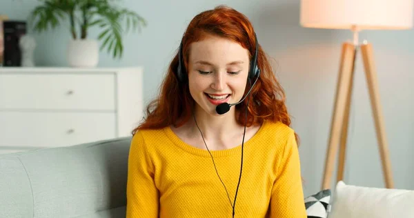 Portret pięknej, wesołej rudej dziewczyny ze słuchawkami za pomocą laptopa. Szczęśliwa kobieta ma rozmowę wideo. — Zdjęcie stockowe