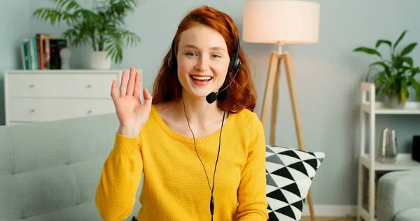 Portret van mooie vrolijke roodharige meisje met headsets hebben video call. — Stockfoto