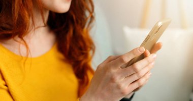 Evdeki güzel, neşeli, kızıl saçlı kızın cep telefonuyla çekilmiş portresini kapat..