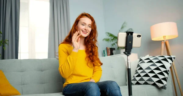 Портрет молодой блоггерши, сидящей на диване и разговаривающей перед веб-камерой смартфона. Девушка тренирует свой блог онлайн из дома. Привлекательная счастливая женщина тренер разговор для видеоблога . — стоковое фото