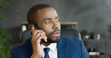 Afro-Amerikalı ciddi iş adamı akıllı telefondan konuşuyor. Erkek, cep telefonuyla konuşuyor..