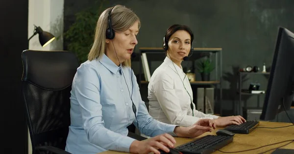 Seniorinnen und junge Betreiberinnen von Callcentern in Headsets arbeiten an Computern im Kundendienstbüro. — Stockfoto