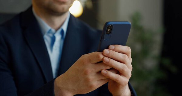 Close up of smartphone in hands. Businessman tapping and scrolling on mobile phone in office.