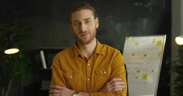 Gros plan de jeune bel homme en chemise jaune debout dans la salle de bureau et regardant la caméra avec un visage sérieux . — Photo