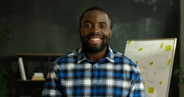 穿着莫斯利衬衫的非洲裔美男子站在办公室里，对着相机开心地微笑的画像. — 图库照片