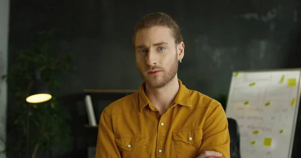 Крупный план молодого красивого мужчины в желтой рубашке, стоящего в офисной комнате и смотрящего в камеру с серьезным лицом . — стоковое фото