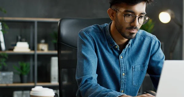 Close up of handsome young Arab busy male office worker sitting at table and working on laptop computer. — Stock Photo, Image