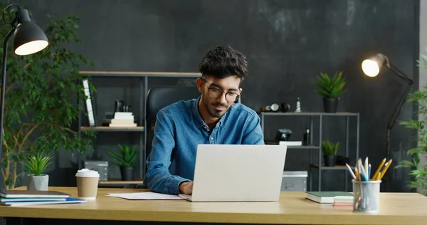 Ung arabisk upptagen manlig kontorsarbetare sitter vid bordet, arbetar på bärbar dator och överväger. — Stockfoto