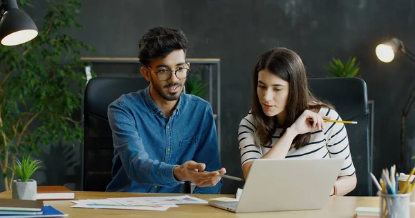 Muliethnic ung kille och flicka sitter vid bordet tillsammans vid laptop dator på kontoret och arbetar över nya start projekt. — Stockfoto