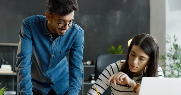 Kafkas kız dizüstü bilgisayarla masada oturuyor ve Arap adam tablet cihazıyla yardım ediyor..