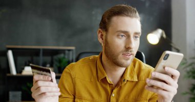 Masada oturan genç bir ofis çalışanı, elinde kredi kartı ve online alışveriş yapıyor..