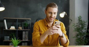 Ofiste elinde akıllı telefonu tutan gülümseyen genç adam..