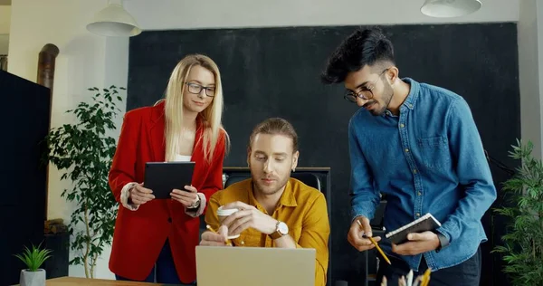 Ung blond vacker kvinna och två blandade raser män pratar och tvistar om affärsstrategi framför bärbar dator på kontoret. — Stockfoto