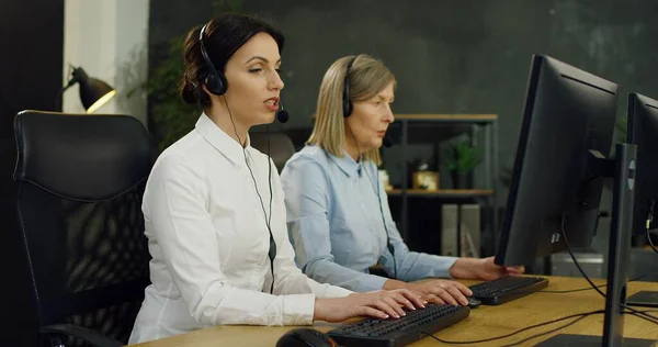 Female customer support worker in wireless headset sitting at computer screen and solving problem of client.