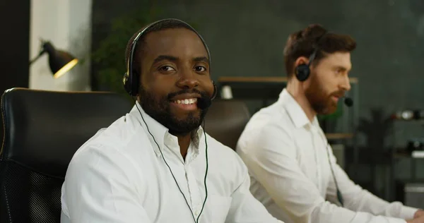 在呼叫中心计算机工作的戴耳机的英俊非洲裔美国年轻人的画像. — 图库照片