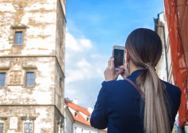 Kadın turist Prag'da güneş ve mavi gökyüzü altında çekim güneşli bir günde elinde onu telefon kamera ile. Prag'da popüler turistik yerlerinden