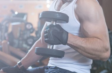 Kaslı vücut geliştirmeci adam spor salonunda dumbbells ile yapıyor