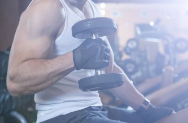 Kaslı vücut geliştirmeci adam spor salonunda dumbbells ile yapıyor