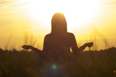 Gün batımında yoga yapan bir kadının arka ışığı.