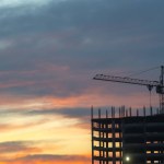 Industriële bouwkranen en bouwsilhouetten boven de zon