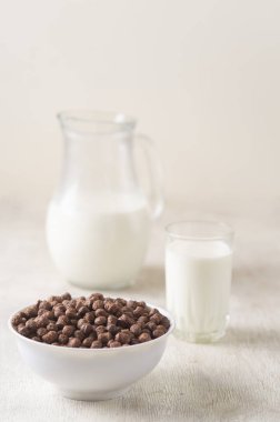 Beyaz ahşap arka planda çikolatalı mısır topu ve süt dolu bir kase..