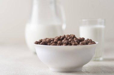 Beyaz ahşap arka planda çikolatalı mısır topu ve süt dolu bir kase..