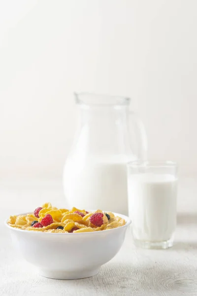 Corn Flakes with berries raspberries, blueberries and currants with milk on white wooden background