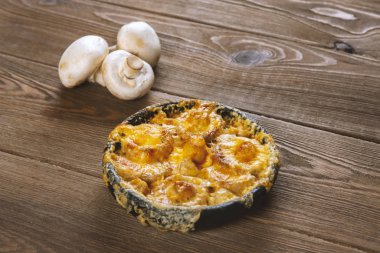 Tahta masada tavada peynir hamuruyla pişirilmiş mantarlar.