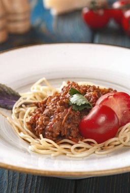 Kıymalı spagetti ve mavi ahşap arka planda vişneli domates..