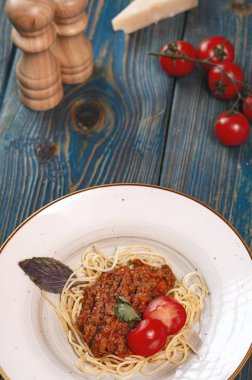 Beyaz tabakta spagetti bolonez makarna, tuz, biber, peynir ve domates mavi ahşap arka planda.