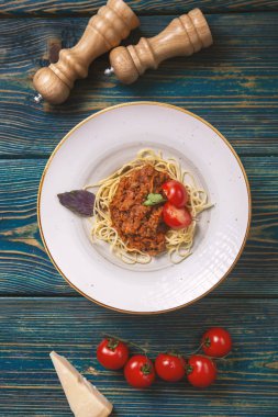 Beyaz tabakta spagetti bolonez makarna, tuz, biber, peynir ve domatesler mavi ahşap arka planda.