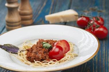Beyaz tabakta spagetti bolonez makarna, tuz, biber, peynir ve domates mavi ahşap arka planda.