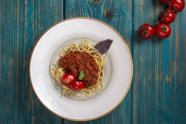 Beyaz tabakta spagetti bolonez makarna, tuz, biber, peynir ve domatesler mavi ahşap arka planda.