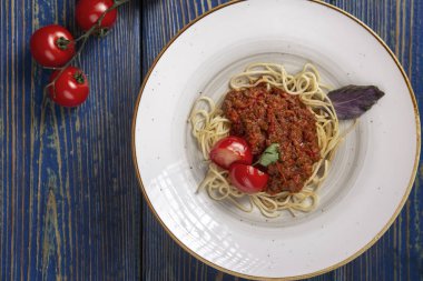 Etli makarna, domates sosu ve mavi ahşap masada sebzeler. en üstteki görünüm