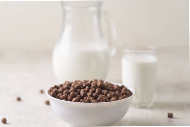 Beyaz ahşap arka planda çikolatalı mısır topu ve süt dolu bir kase..
