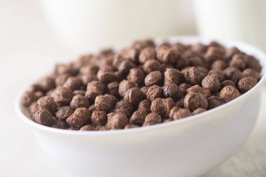 Beyaz ahşap arka planda çikolatalı mısır topu ve süt dolu bir kase..