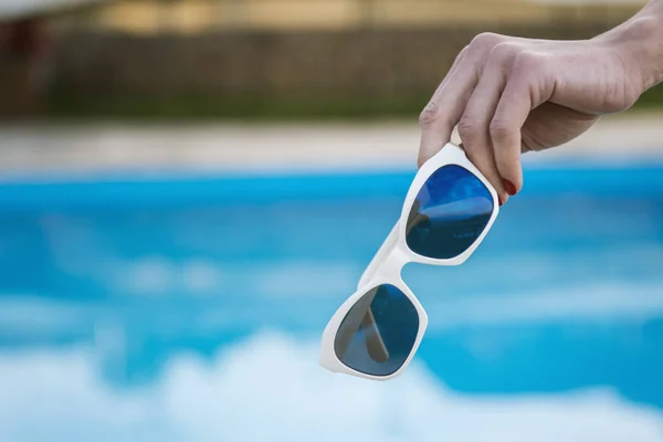 Woman hand holding sunglasses and lying on deckchair by the swim — Stock Photo, Image