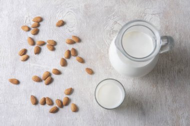 Badem ve süt bir sürahide ve beyaz ahşap bir arka planda bir bardak.