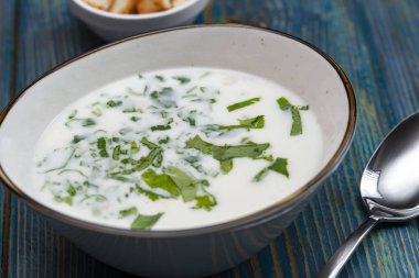 Yoğurt çorbası, mavi ahşap bir masada otlar ve krakerler.