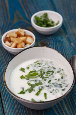 Yoğurt çorbası, mavi ahşap bir masada otlar ve krakerler.